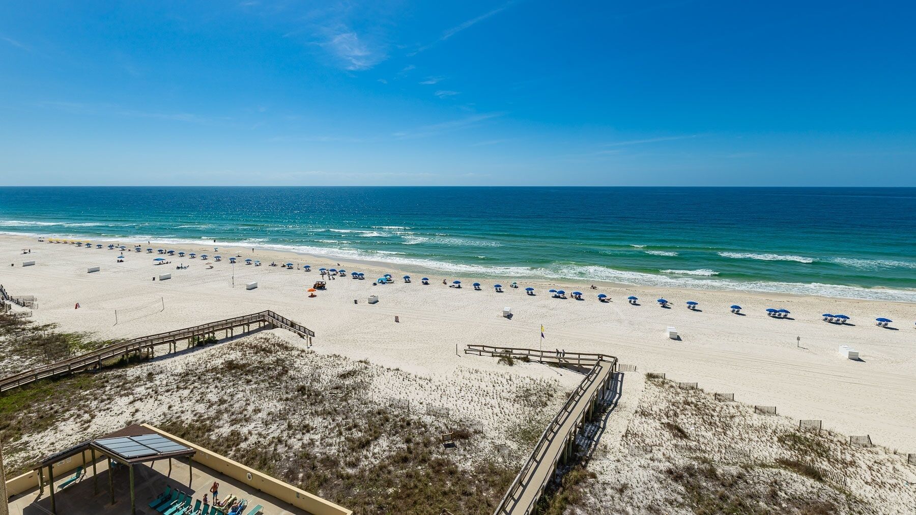 A beach with a wooden walkway leading to a building with a glass roof, overlooking the ocean.
