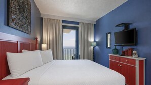 Ein Hotelzimmer mit einem großen Bett, einem Fernseher, einer roten Kommode und Blick auf das Meer.