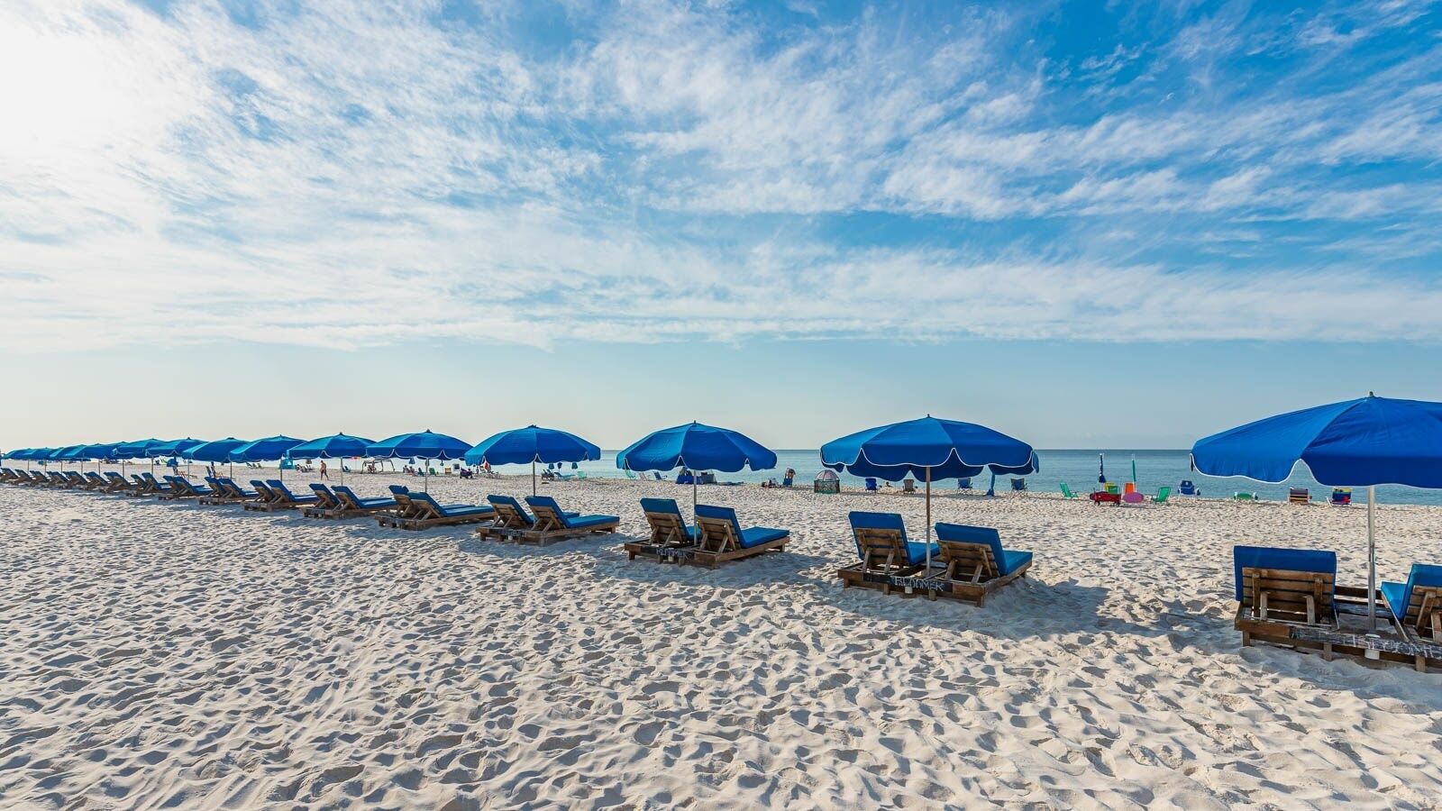 A beach with rows of sun loungers and blue umbrellas.