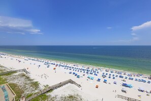 Une plage avec une promenade en bois menant à l’eau, un ciel dégagé et des parasols sur le sable.