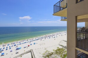 A beach view from a balcony with a clear sky, a sandy beach with umbrellas, and the ocean. - Phoenix I 1145 2 Bedroom Condo (Orange Beach)