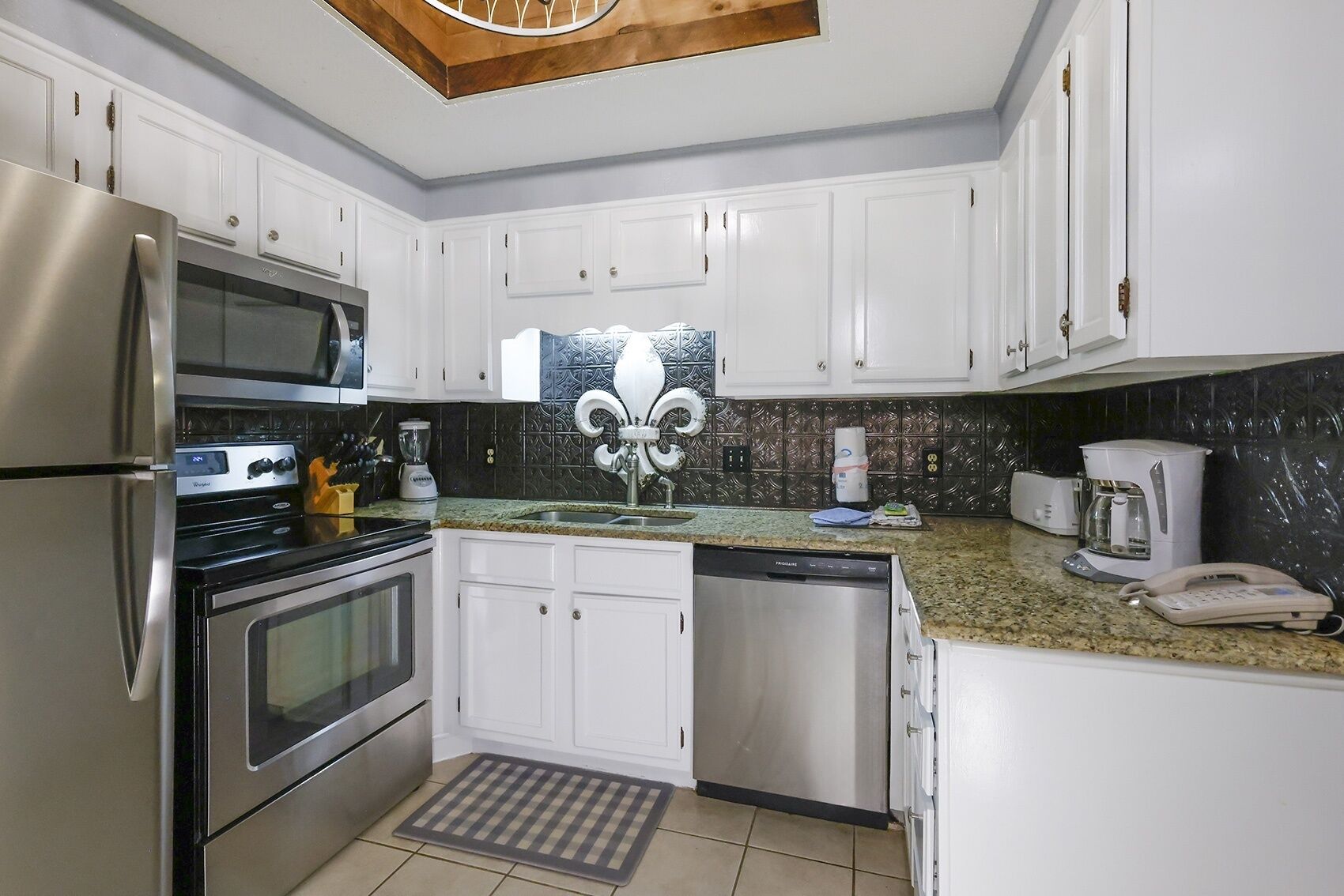 A modern kitchen with stainless steel appliances, white cabinetry, and a patterned backsplash.