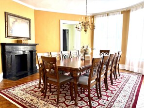 A dining room with a wooden table, chairs, a chandelier, a fireplace, and a patterned rug. - Charming Victorian Duplex 4br Sleeps 10 3 Bedroom Home (Niagara Falls)