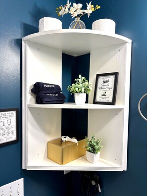 Une étagère de salle de bain avec un porte-serviettes, un cadre décoratif, une plante en pot et une boîte.