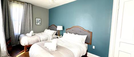 A hotel room with two beds, a ceiling fan, a nightstand with a lamp, and a door.