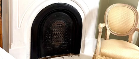 A white fireplace with a black door, a decorative shield, and a small white vase with flowers on top.