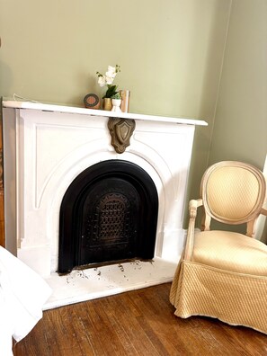 Une cheminée blanche avec une porte noire, un écusson décoratif et un petit vase blanc orné de fleurs.