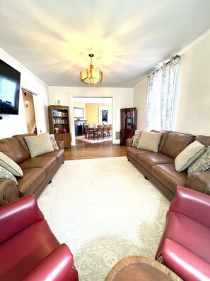 A living room with two leather sofas, a red armchair, a chandelier, a television, and a dining area in the background. - Charming Victorian Duplex 4br Sleeps 10 3 Bedroom Home (Niagara Falls)