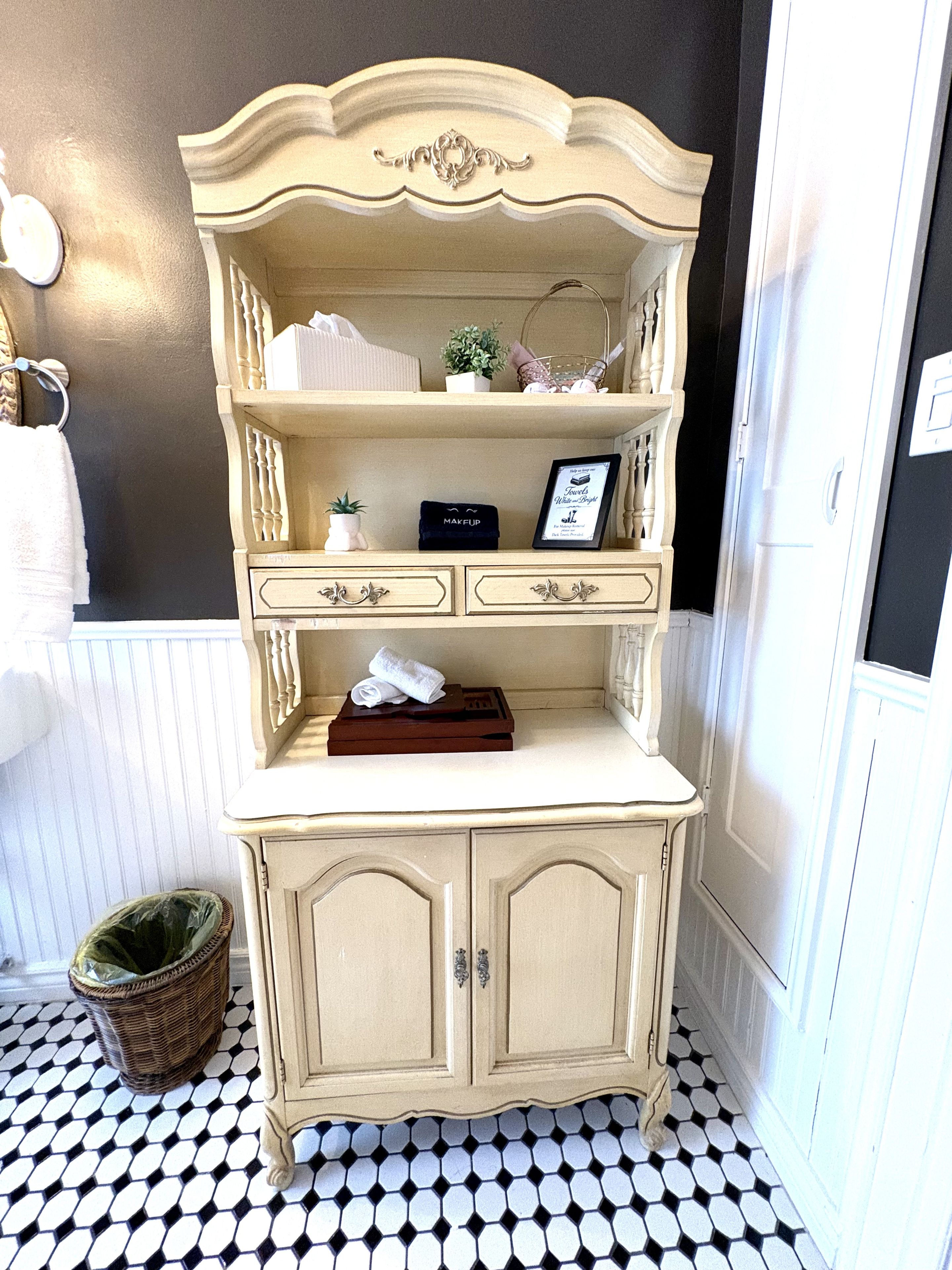 Un tocador de estilo vintage con espejo, repisas con objetos decorativos y una pequeña planta.
