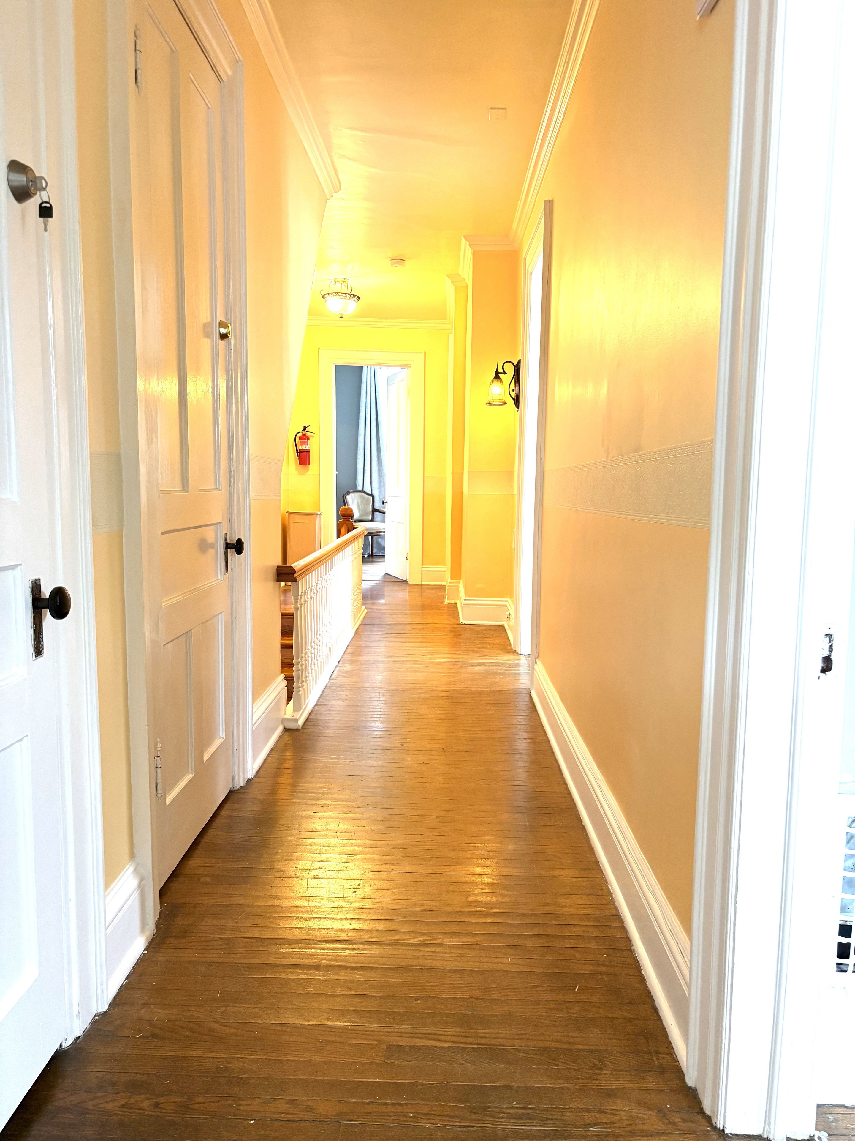 A hallway with wooden flooring, white doors, and a staircase with a railing.