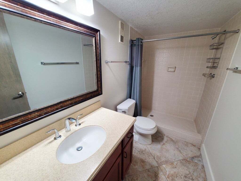 A bathroom with a sink, mirror, toilet, and shower area.