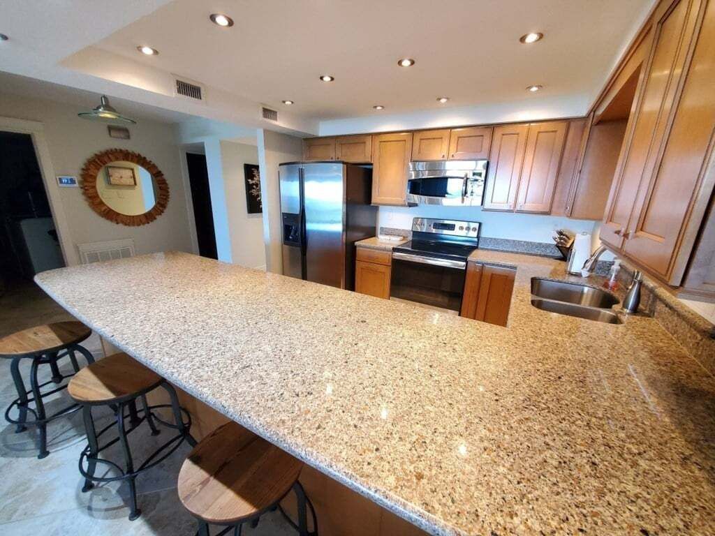 A kitchen with granite countertops, stainless steel appliances, wooden cabinets, and a central island with bar stools.