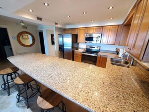 Eine Küche mit Granit Arbeitsplatten, Edelstahlgeräten, Holzschränken und einer zentralen Kochinsel mit Barhocker.