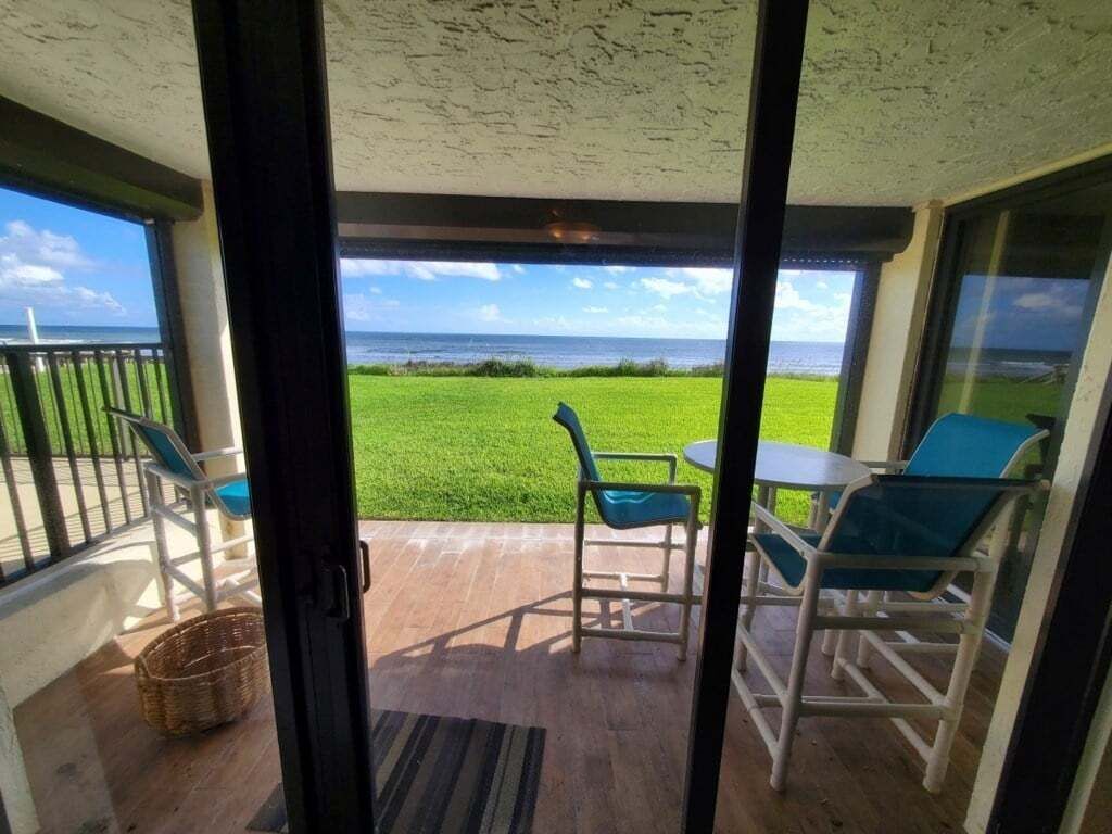 A covered outdoor area with a view of the ocean, a grassy lawn, and a table with chairs.