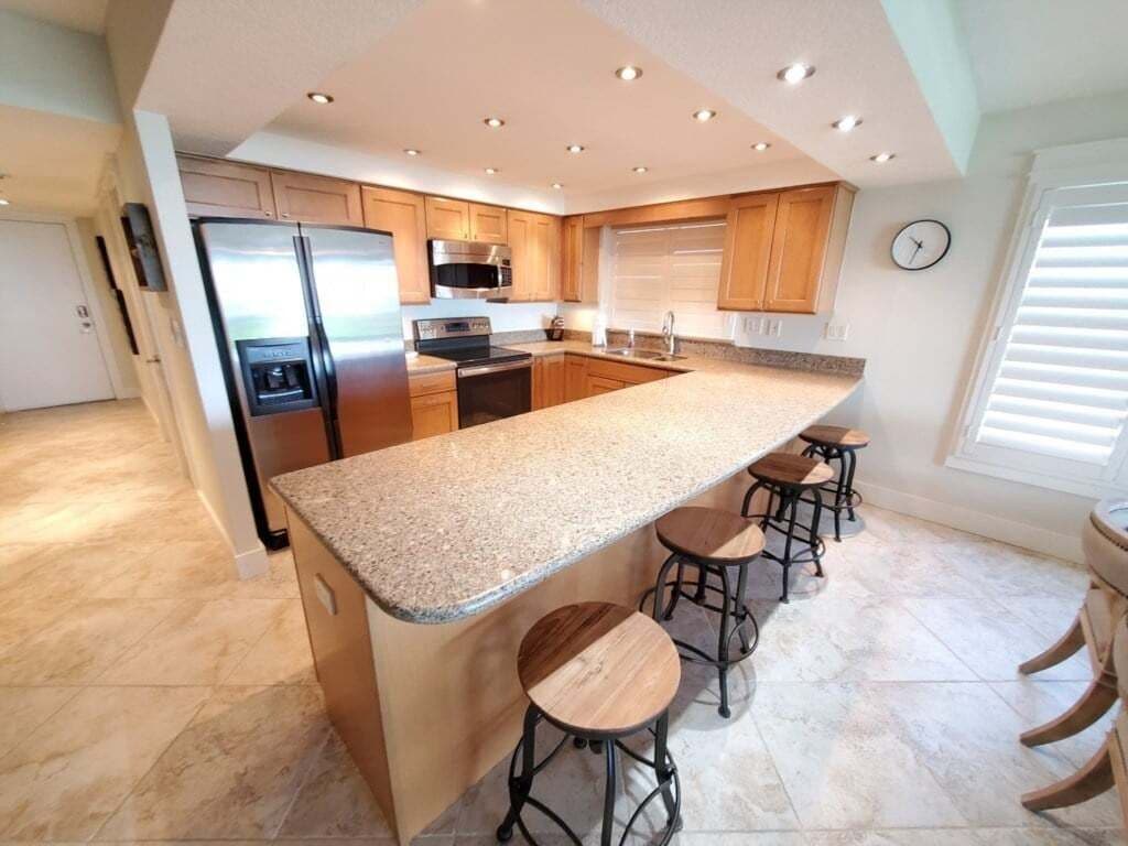 Uma cozinha moderna com bancada de granito, eletrodomésticos de aço inoxidável, armários de madeira e banquetas.