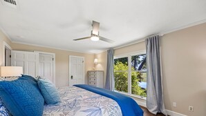 A bedroom with a large bed, a ceiling fan, a dresser, a window with curtains, and a view of greenery outside. - 1826 Highland Drive 3 Bedroom Home (Fernandina Beach)