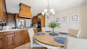 A modern kitchen with wooden cabinets, stainless steel appliances, and a dining area with a round table and chairs. - 1826 Highland Drive 3 Bedroom Home (Fernandina Beach)