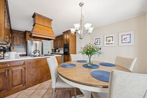 A modern kitchen with wooden cabinets, stainless steel appliances, and a dining area with a round table and chairs. - 1826 Highland Drive 3 Bedroom Home (Fernandina Beach)
