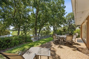An outdoor patio with a table and chairs, surrounded by trees and a view of a water body. - 1826 Highland Drive 3 Bedroom Home (Fernandina Beach)
