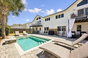 Ein zweistöckiges Haus mit Swimmingpool, Sitzgelegenheiten im Freien und einer Holzterrasse.