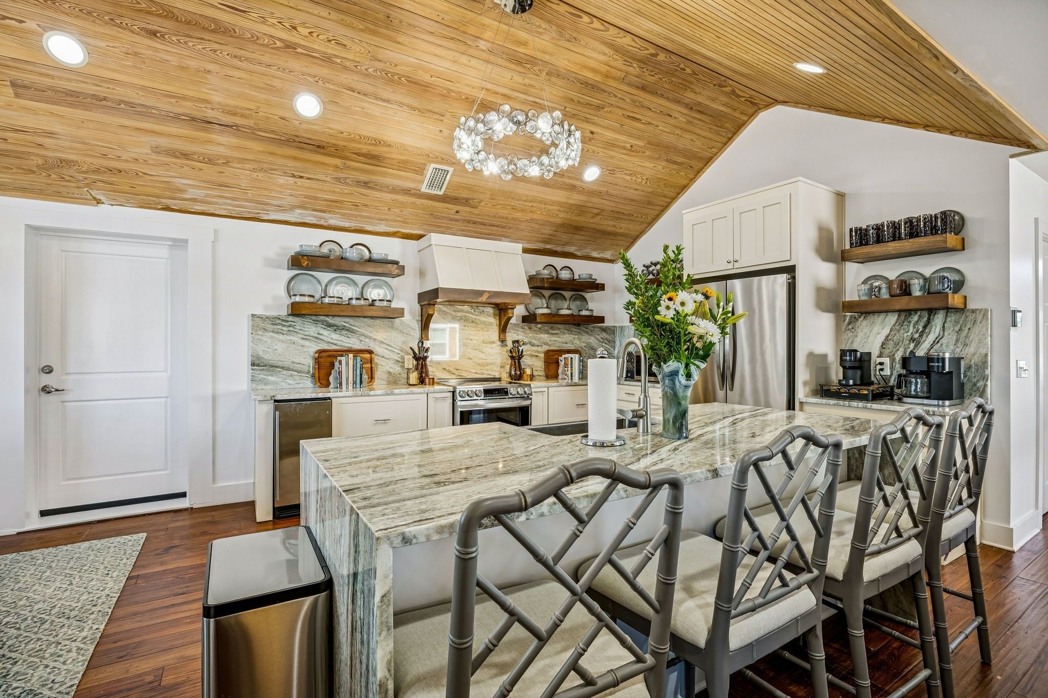 A modern kitchen with a marble island, wooden ceiling, and built-in appliances.