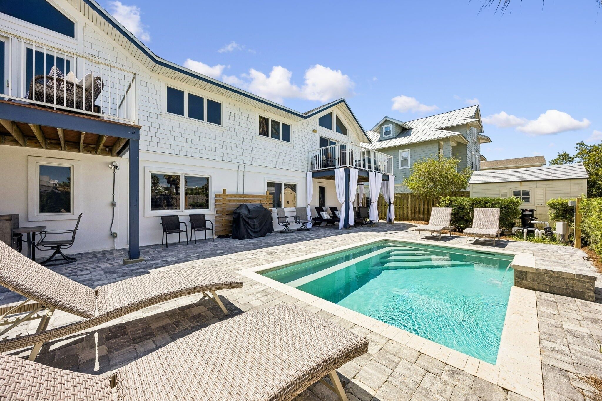 A residential property with a swimming pool, outdoor seating, and a covered patio area.
