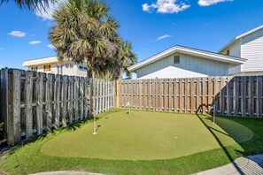 A backyard with a wooden fence, a palm tree, and a golf putting green. - 733a And B Tarpon Avenue 6 Bedroom Home (Fernandina Beach)