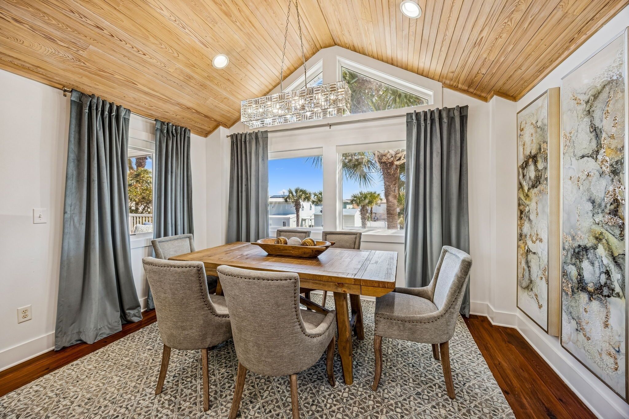 A dining area with a wooden table, four upholstered chairs, and a chandelier.