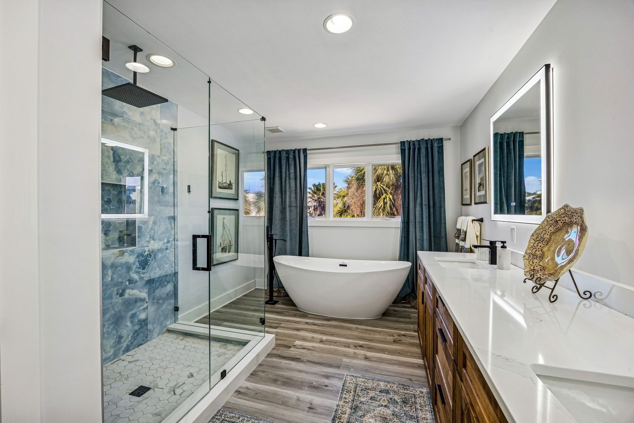 A modern bathroom with a freestanding bathtub, glass shower enclosure, and a large window with curtains.