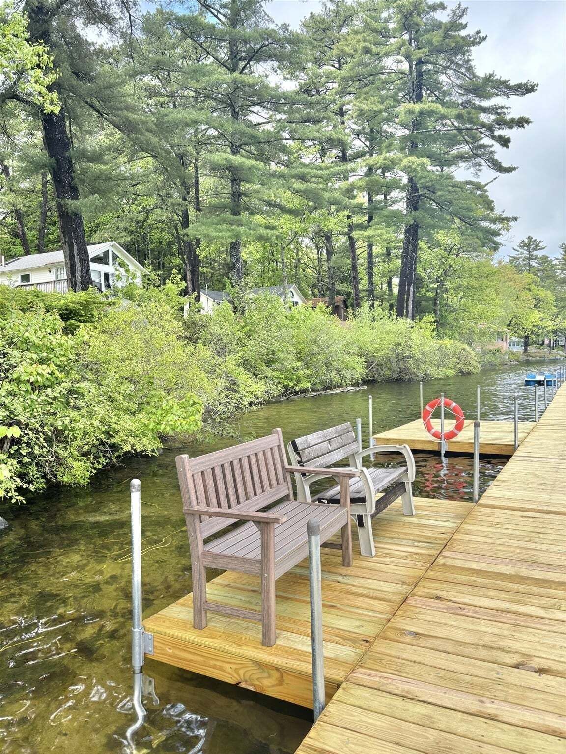 A wooden dock extending into a body of water, with two benches and a lifebuoy on the dock.