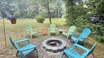 A fire pit surrounded by outdoor seating, with trees and a clear sky in the background.