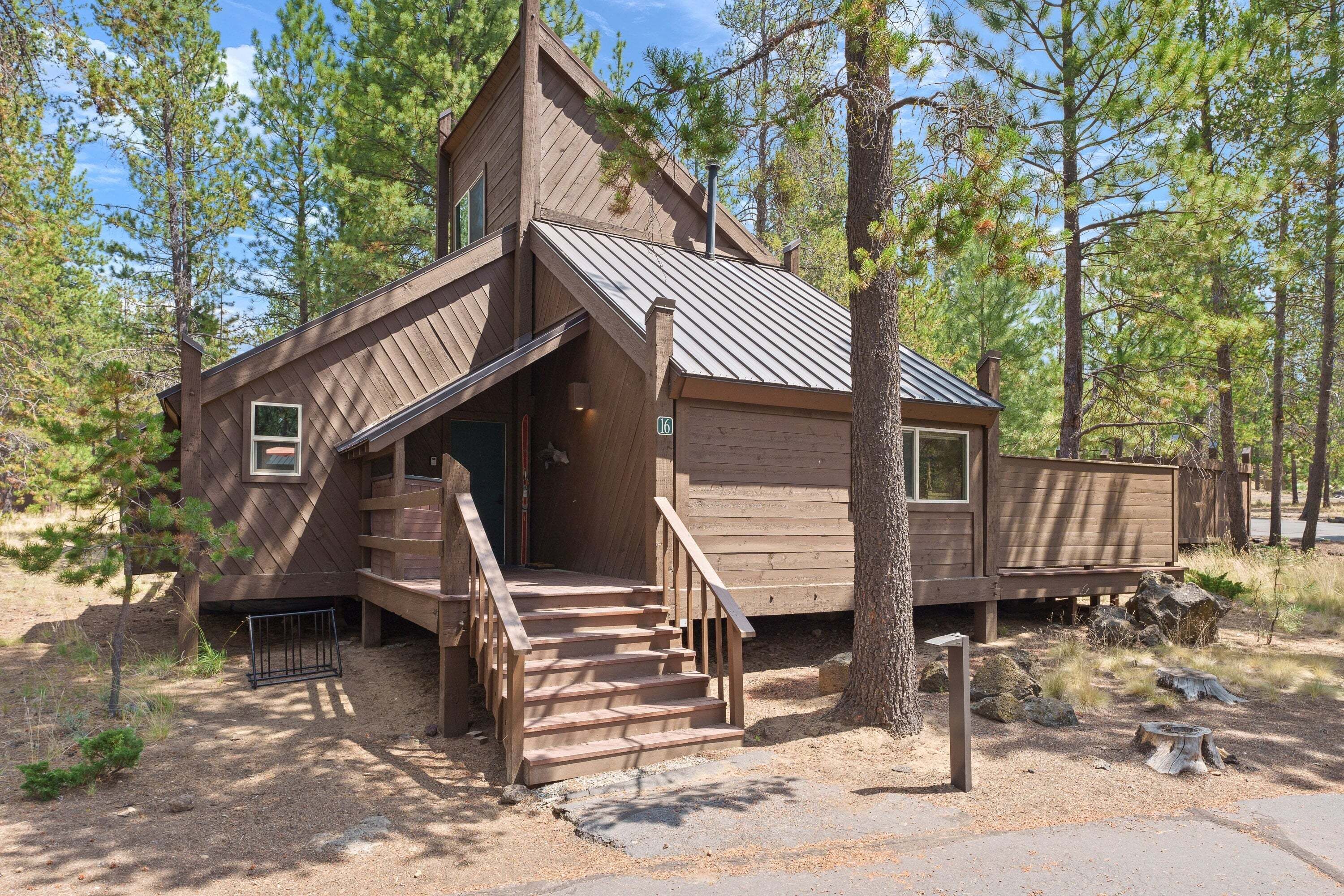 A wooden cabin with a steeply pitched roof, a front porch with stairs, and a small window.