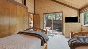 Ein Ferienhaus-Innenraum mit zwei Holzbetten, einem Fernseher auf einer Kommode und einer Schiebetür zu einem Außenbereich.