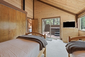 A cabin interior with two wooden beds, a TV on a dresser, and a sliding glass door leading to an outdoor area. - 16 Pole House 2 Bedroom Home (Bend)