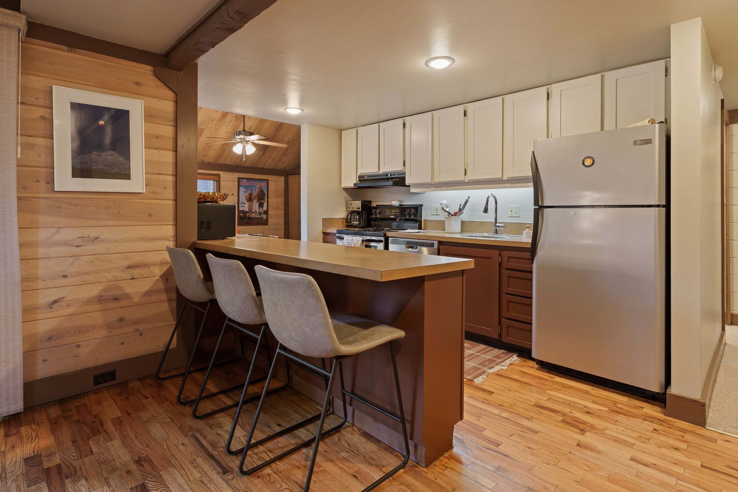 A kitchen with a wooden island, bar stools, a refrigerator, and wooden cabinetry.