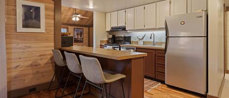 A kitchen with a wooden island, bar stools, a refrigerator, and wooden cabinetry.