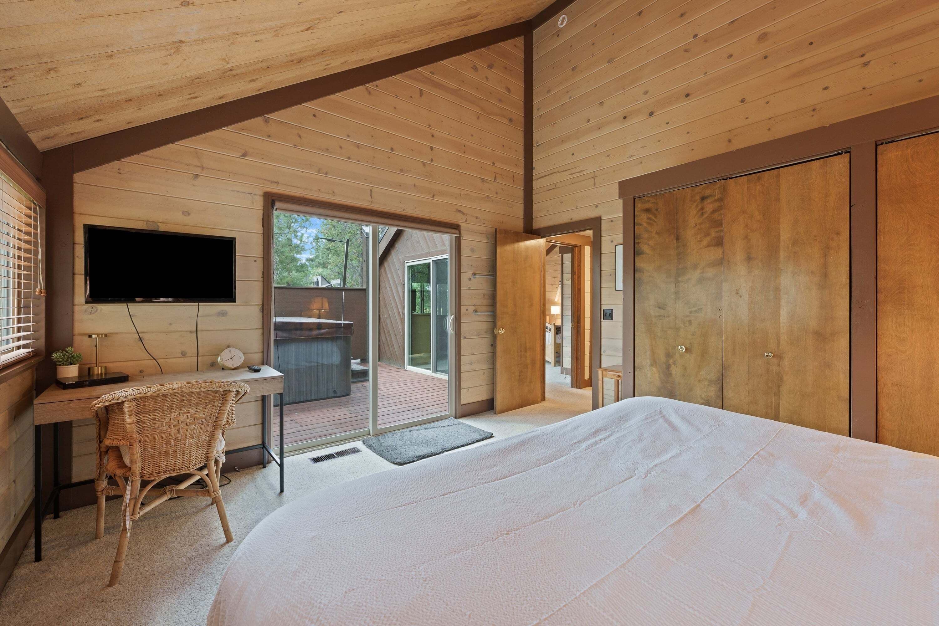 A bedroom with a large bed, a desk with a chair, a television, and a sliding glass door leading to an outdoor area.