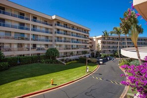 A multi-story hotel with a flat facade, balconies, and a parking area with a fire hydrant. - Maui Banyan H502 1 Bedroom Condo (Kihei)