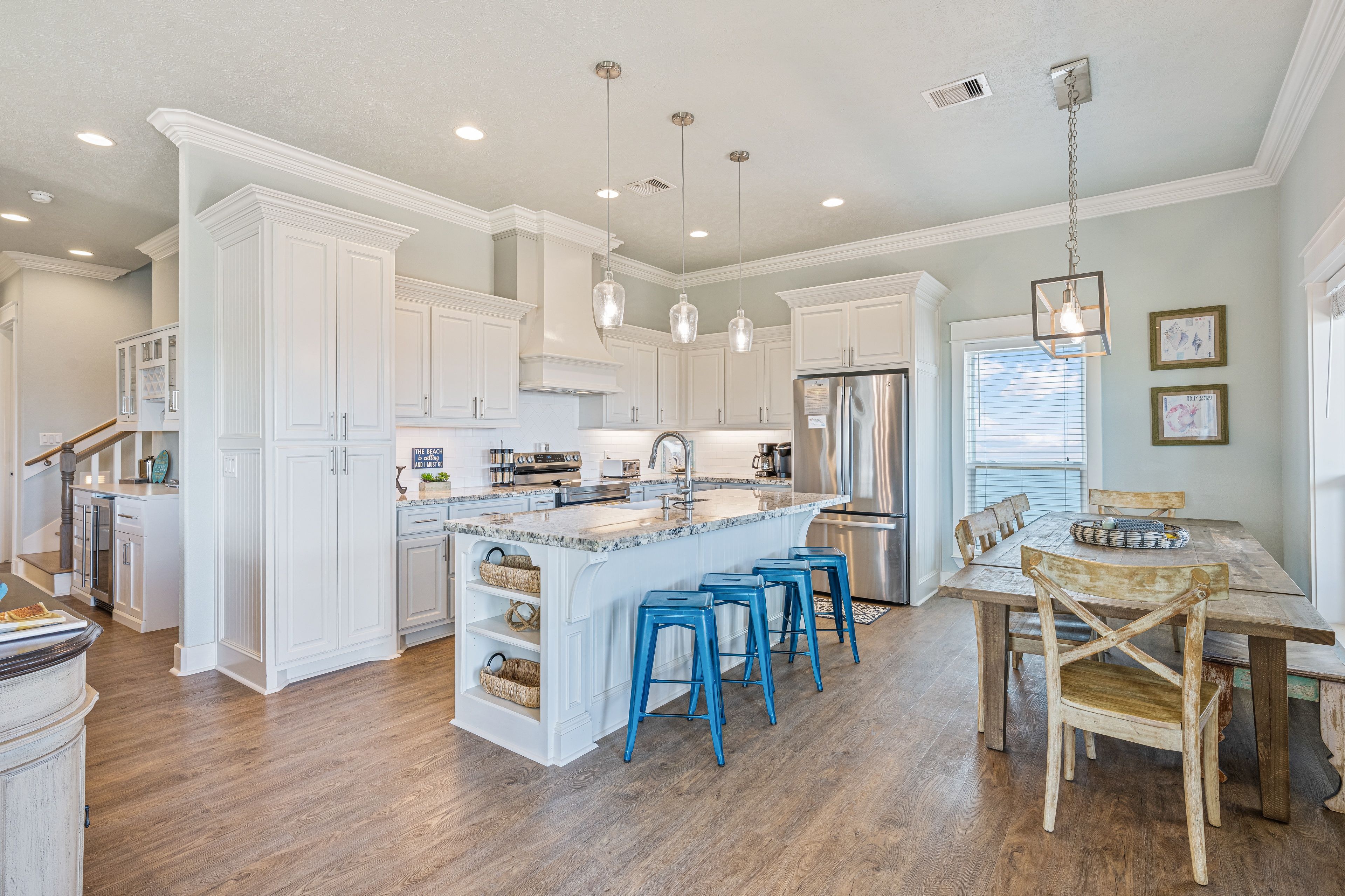 A spacious kitchen with white cabinetry, a central island with stools, stainless steel appliances, and pendant lighting.