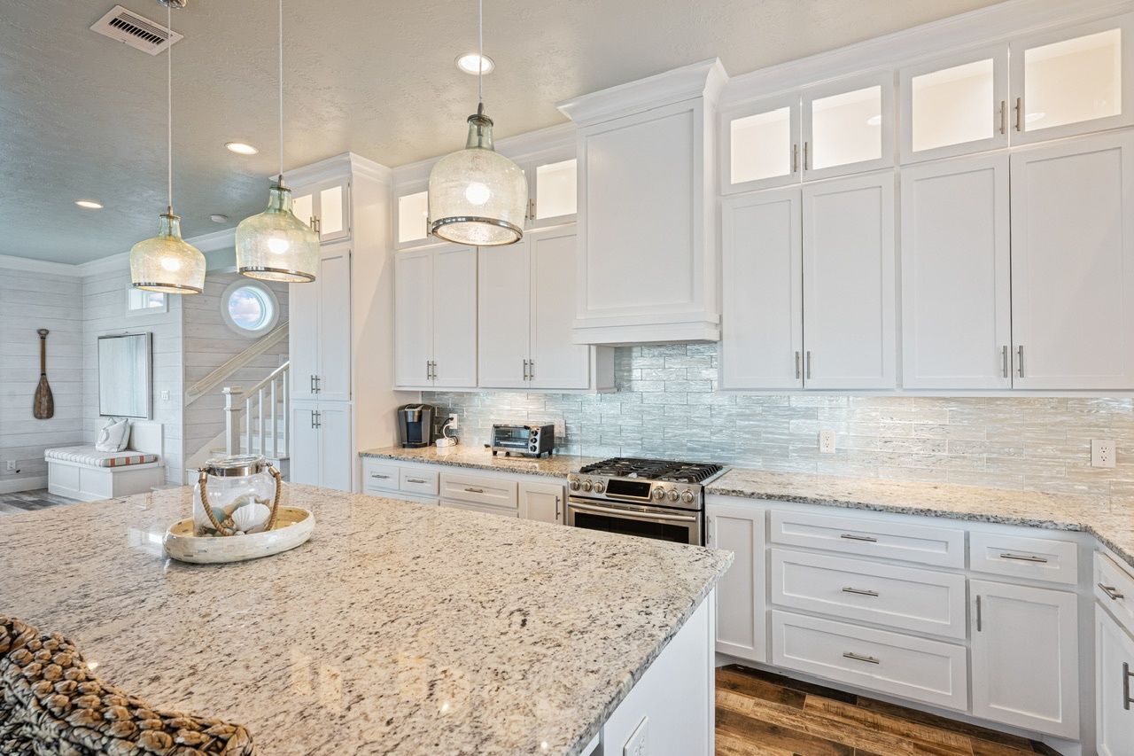 A kitchen with white cabinets, granite countertops, and pendant lighting.