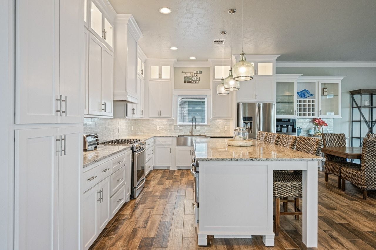 A modern kitchen with white cabinetry, a central island, and a dining area with patterned chairs.