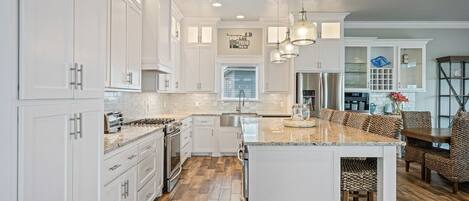 A modern kitchen with white cabinetry, a central island, and a dining area with patterned chairs.