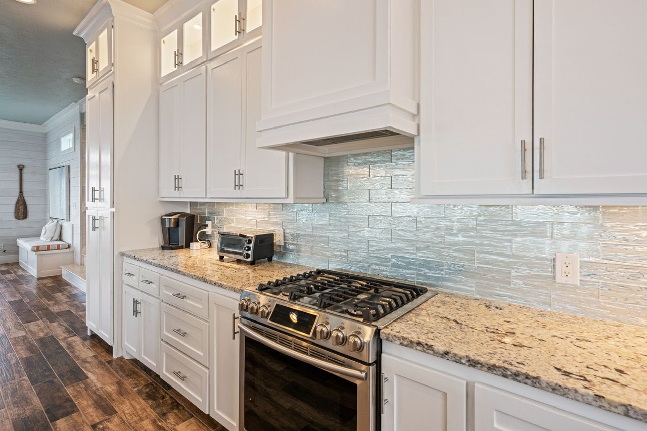 A kitchen with white cabinets, a granite countertop, a gas stove, and a toaster.