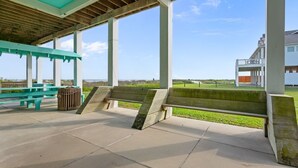 Un espacio al aire libre techado con bancos y mesas de picnic, un cubo de basura y vistas a la playa y al océano.