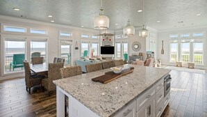 Una cocina amplia con una isla grande, comedor con sillas de mimbre y vistas al exterior.