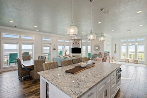 A spacious kitchen with a large island, dining area with wicker chairs, and a view of the outdoors. - Gabriels Landing 5 Bedroom Home (Port Bolivar)