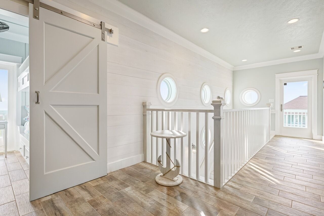 A hallway with a white door, a white railing, and a round table.