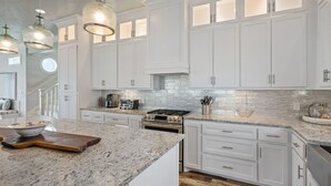 Una cocina moderna con armarios blancos, encimeras de granito e iluminación colgante.