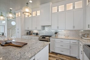 A modern kitchen with white cabinetry, granite countertops, and pendant lighting. - Gabriels Landing 5 Bedroom Home (Port Bolivar)