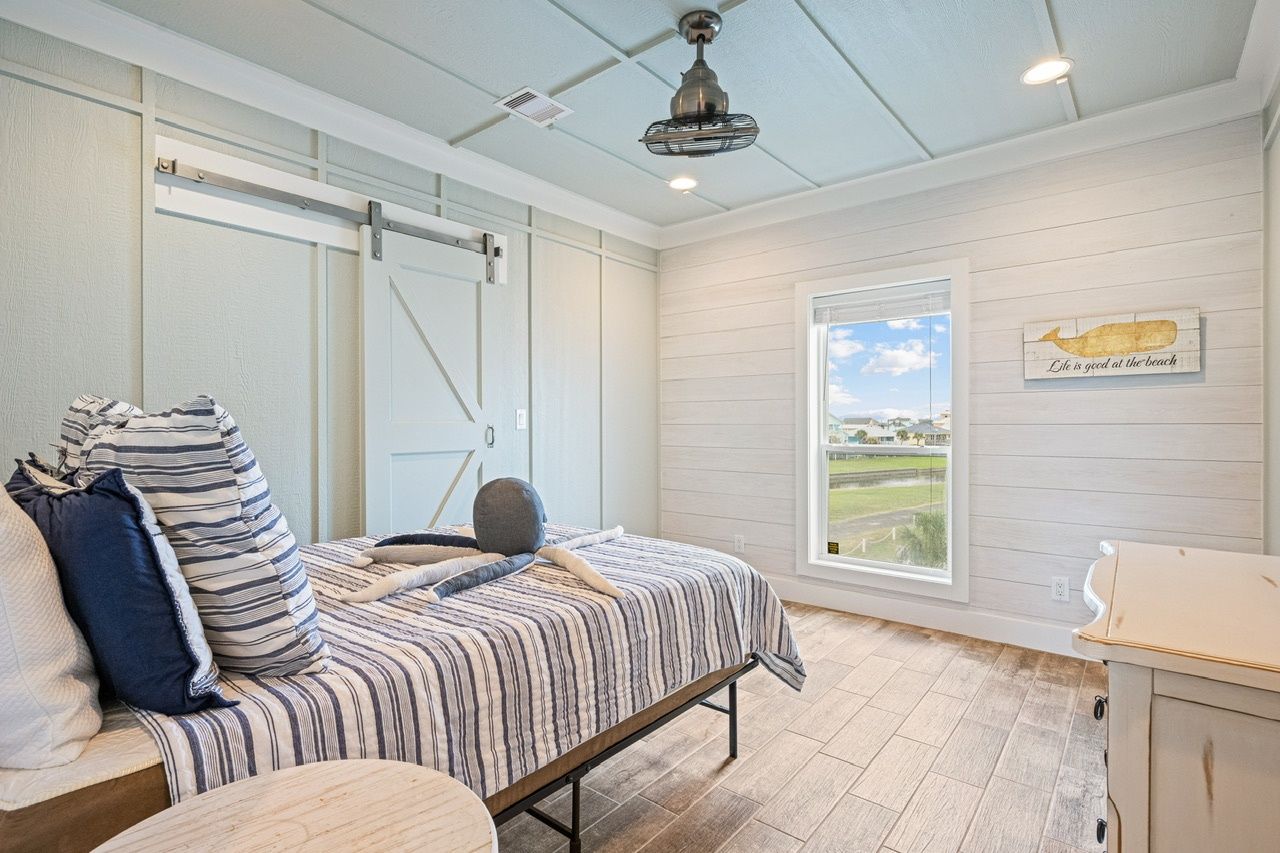 A bedroom with a bed, a window with a view, a ceiling fan, and a wall-mounted light fixture.